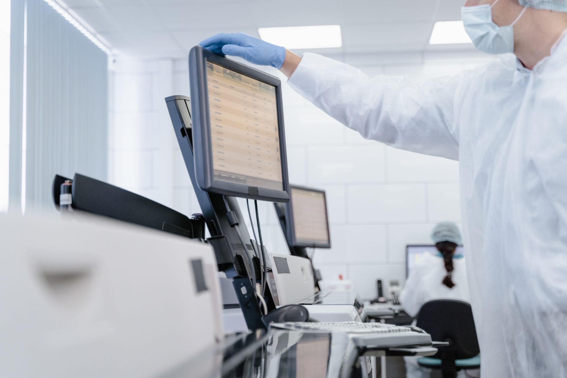 Researcher in protective clothing reaching up to a screen full of data in a bright, modern laboratory